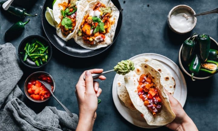 Assembling vegan tacos full of bright colored fillings on a dark background